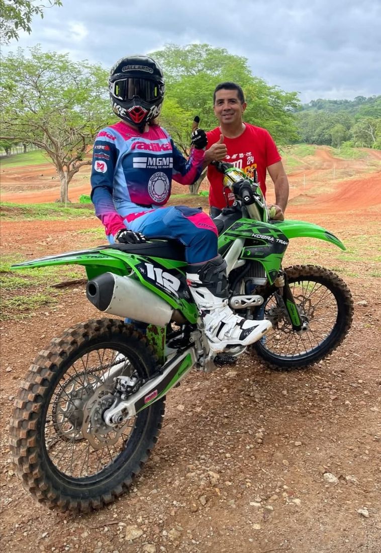 Una piloto con equipación sobre su moto de motocross recién puesta a punto, junto a Oriel Peregrina